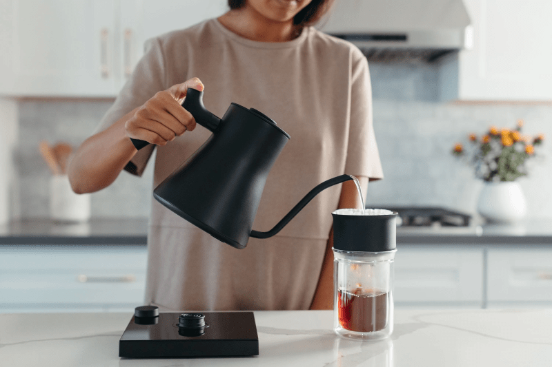 Woman using the matte black Fellow Stagg EKG Electric Kettle to pour coffee