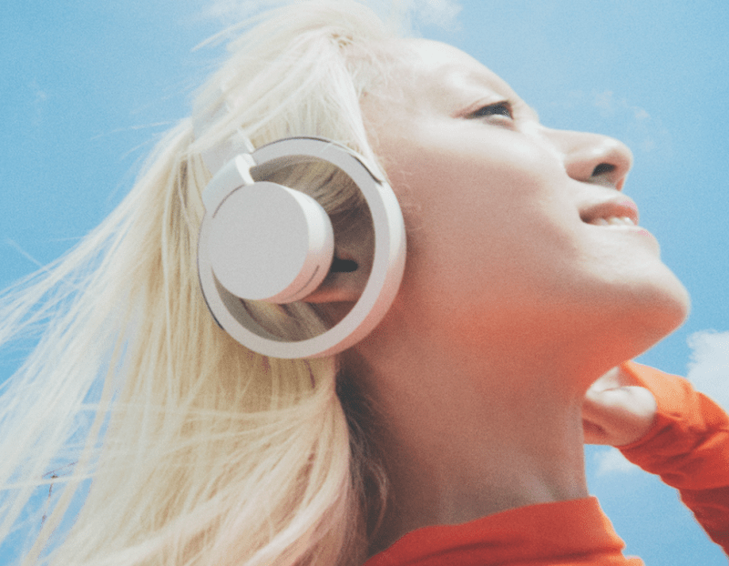 A model wearing nwm ONE Wireless Open-Ear Headphones while walking in a park, enjoying music and ambient sounds.