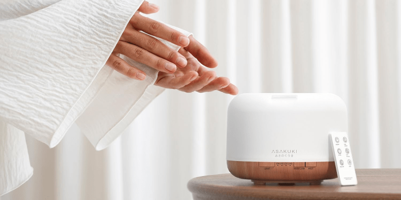 Woman practicing yoga beside an ASAKUKI diffuser in a calm studio