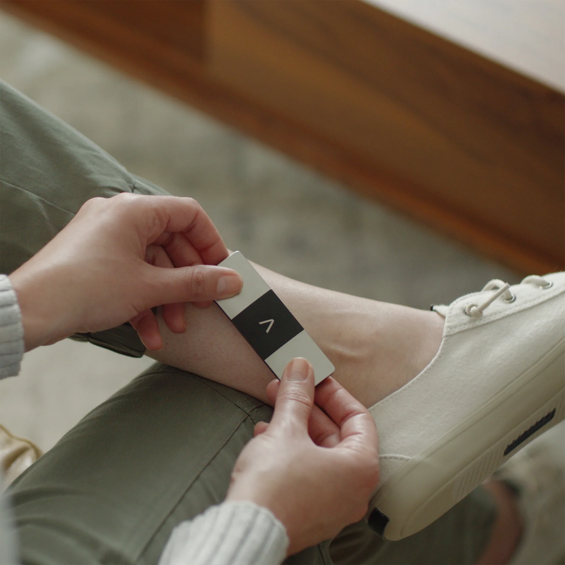Person using KardiaMobile 6L with fingers on two sensors and third sensor touching the left leg.