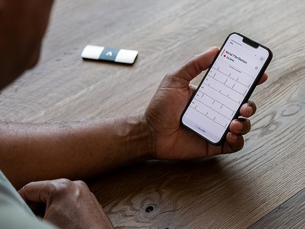 KardiaMobile 6L device next to a smartphone displaying a 6-lead EKG reading in the Kardia app.