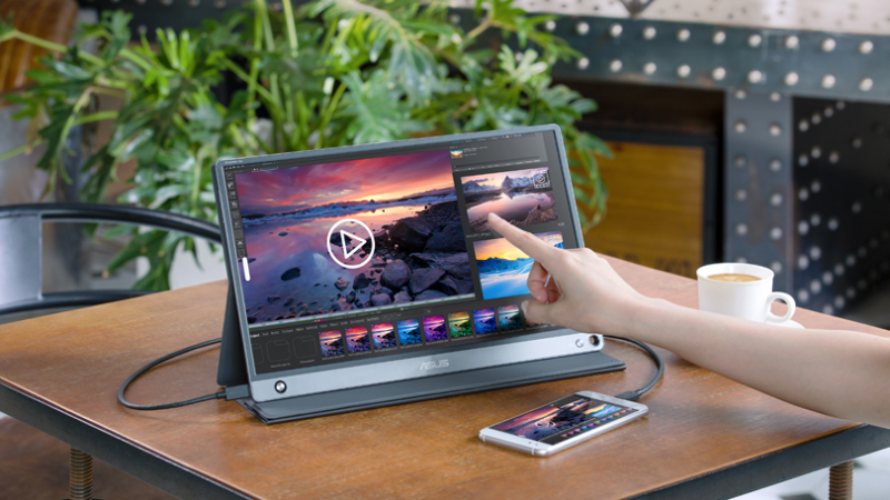 A person working on a laptop with the ASUS ZenScreen Go Wireless set up wirelessly next to it on a table in a bright cafe, showing a mobile dual-monitor setup.
