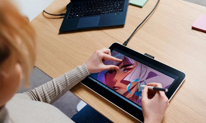 The MovinkPad Pro 14 sitting on a desk stand, connected via a single USB-C cable to a laptop/monitor setup, displaying the Adobe Photoshop desktop interface.