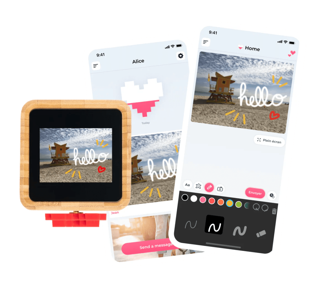 A smartphone on a wooden table displaying the Lovebox app interface with a hand drawing a digital heart, sitting next to the physical wooden Lovebox unit.